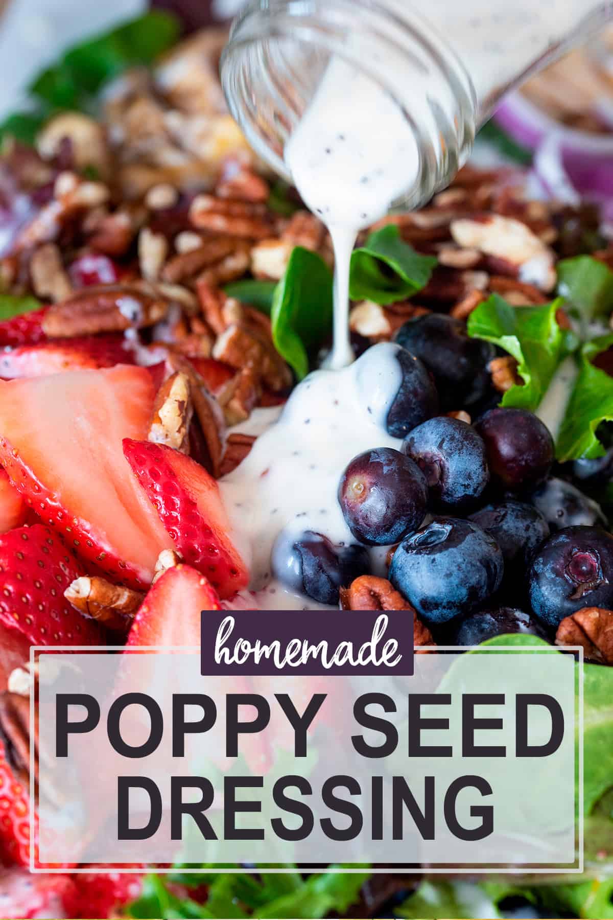 Bottle of creamy poppy seed salad dressing pouring over a salad with strawberry, blueberry, and nuts.