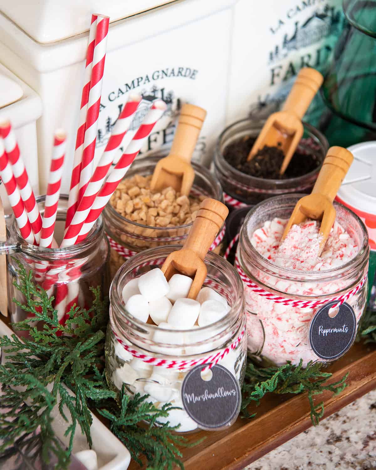 Christmas hot cocoa bar closeup with spoons in mason jars of marshmallows, mints, and candy bits.
