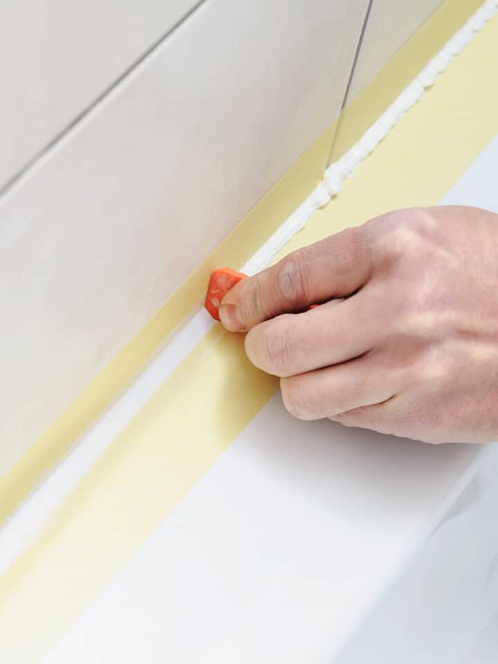 Hand smoothing out caulk on a bathtub surround.