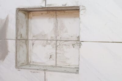 A shower shelf with grout being added in the tiles but no trim.