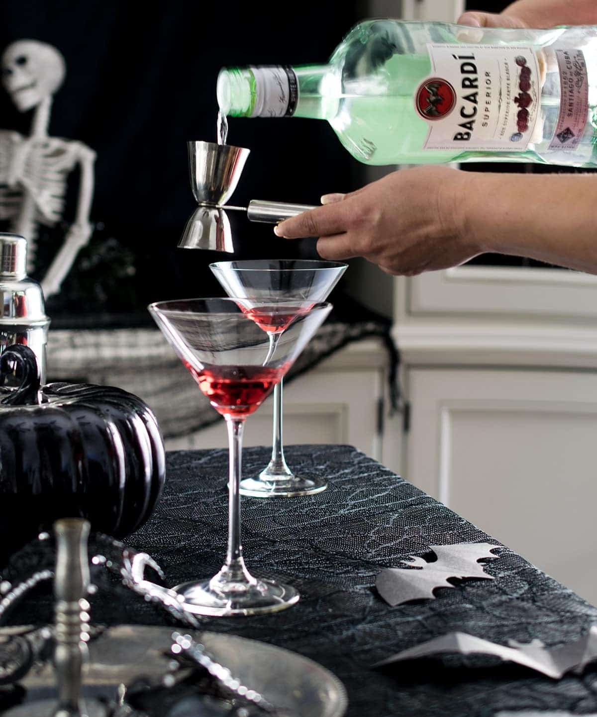 Making a layered cocktail by pouring rum in jigger over grenadine in a martini glass.