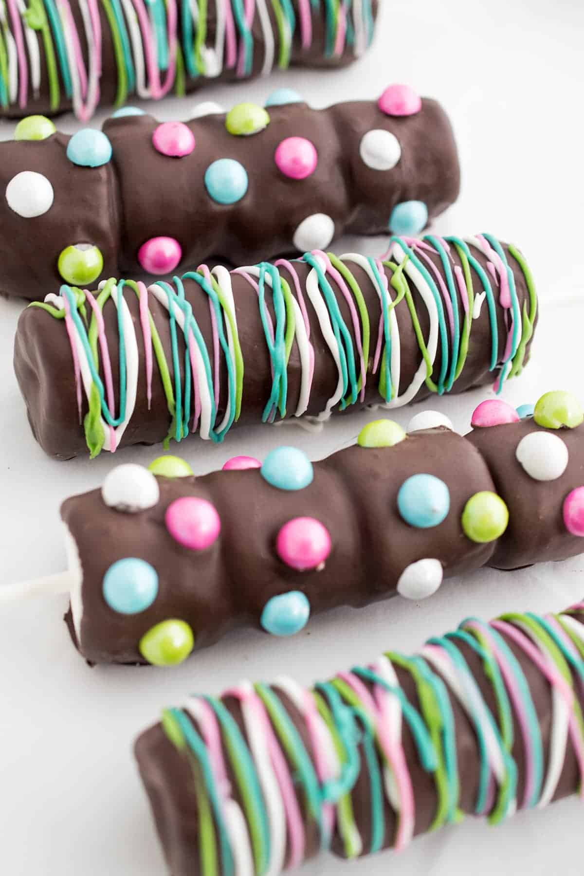 Four marshmallow pops with bright decorations including candies, sprinkles, and melted chocolate.
