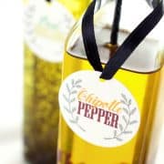 Closeup of printed chipotle pepper label tide to bottle of infused oil with black ribbon with basil oregano oil in background.
