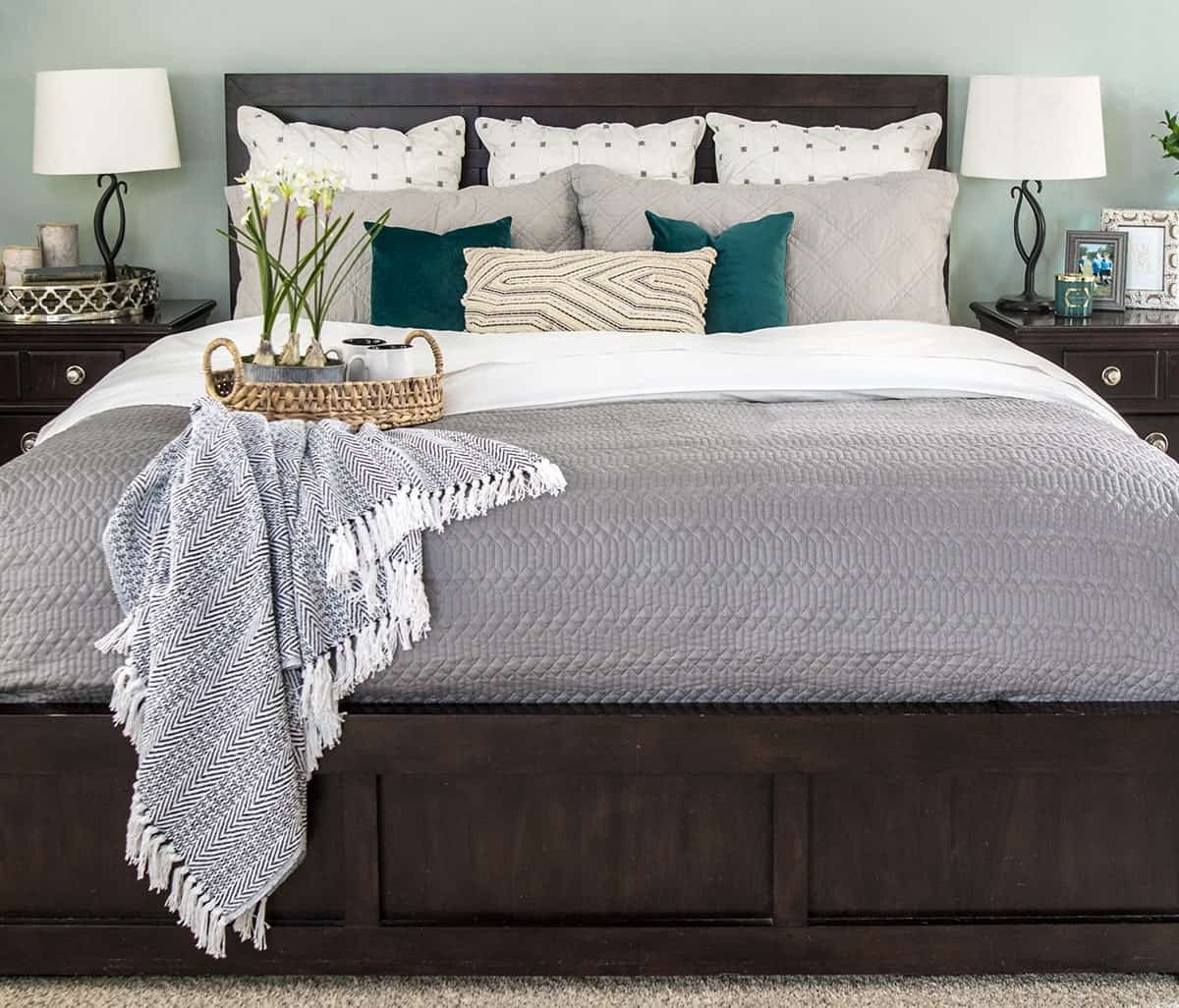 Cozy bed with gray quilt over white sheets. Layered neutral accent pillows with pops of green.
