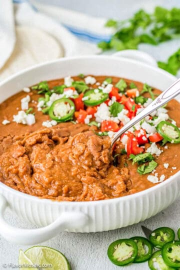 A large pot of refried beans with jalapenos, cheese, and peppers on top.