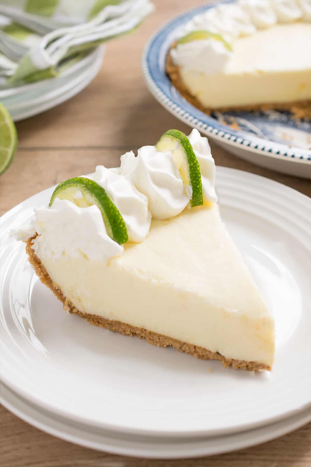 Key lime pie slice on stacked white plate with fresh whipped cream and lime slices.