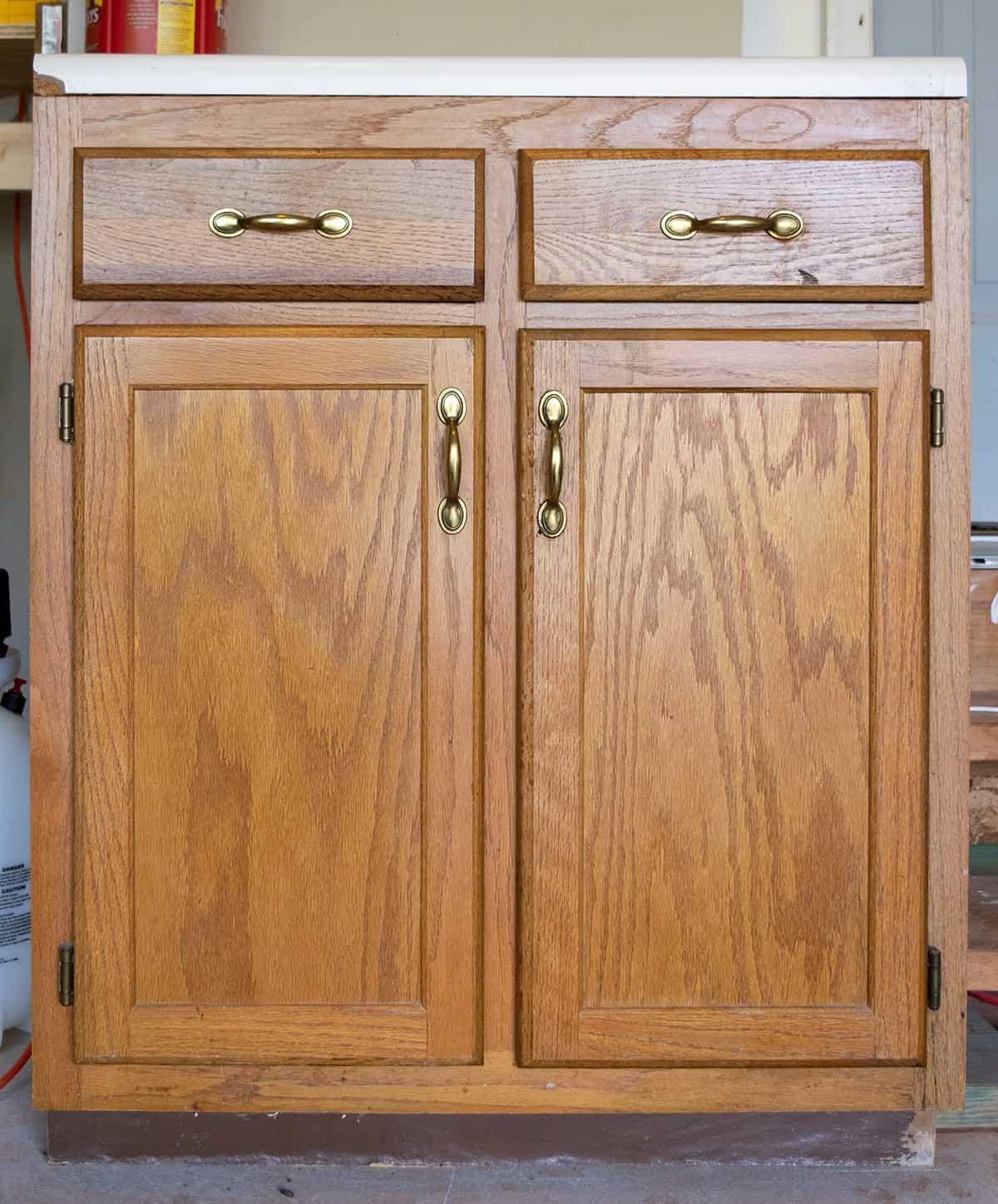 Old oak wood kitchen cabinet section with brass hardware with coffee canister on top.