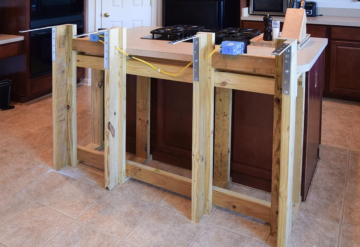 Dark wood kitchen island with beige countertop with wood frame built out for breakfast bar add on.