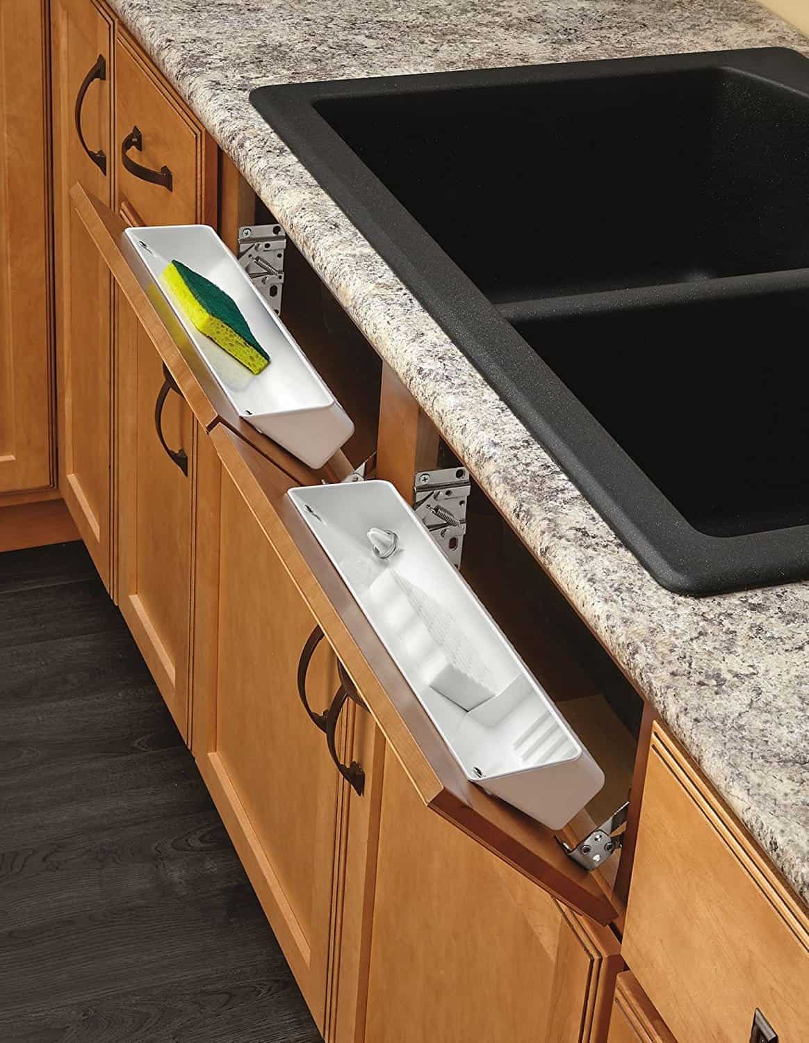 White hinged trays installed inside kitchen sink cabinets for storing sponges and soap/