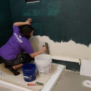 Woman laying mortar for tiling a wall and scraping away excess.