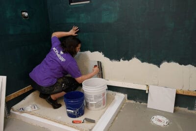Woman laying mortar for tiling a wall and scraping away excess.