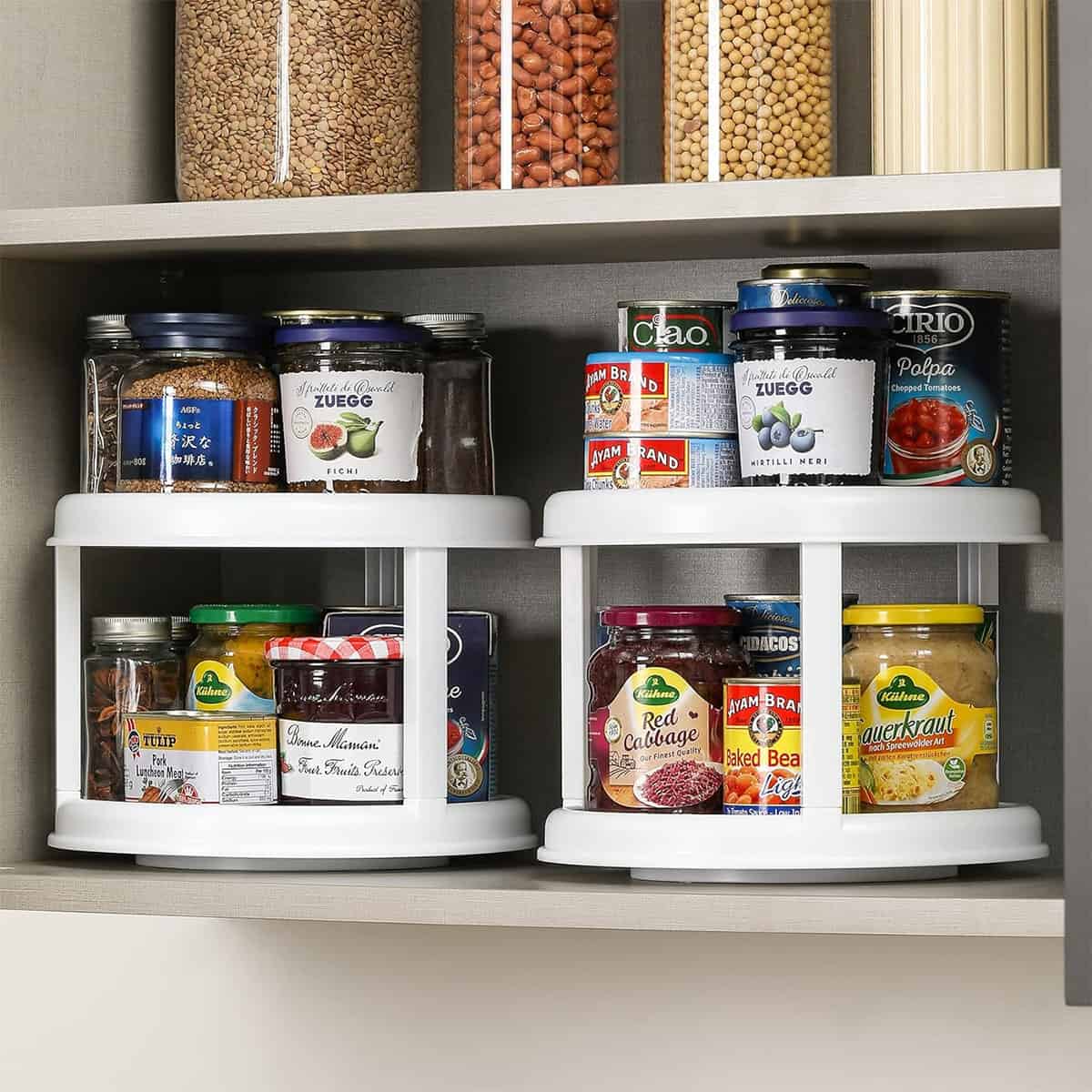 Two lazy Susan organizers with condiments on them inside a kitchen cabinet.