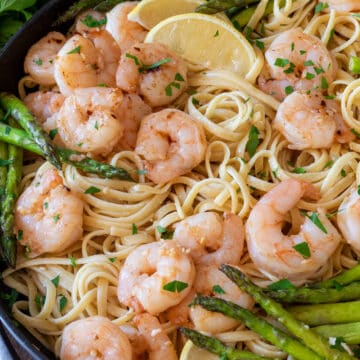 Lemon shrimp asparagus pasta in a black pan with lemon slices and parmesan cheese.