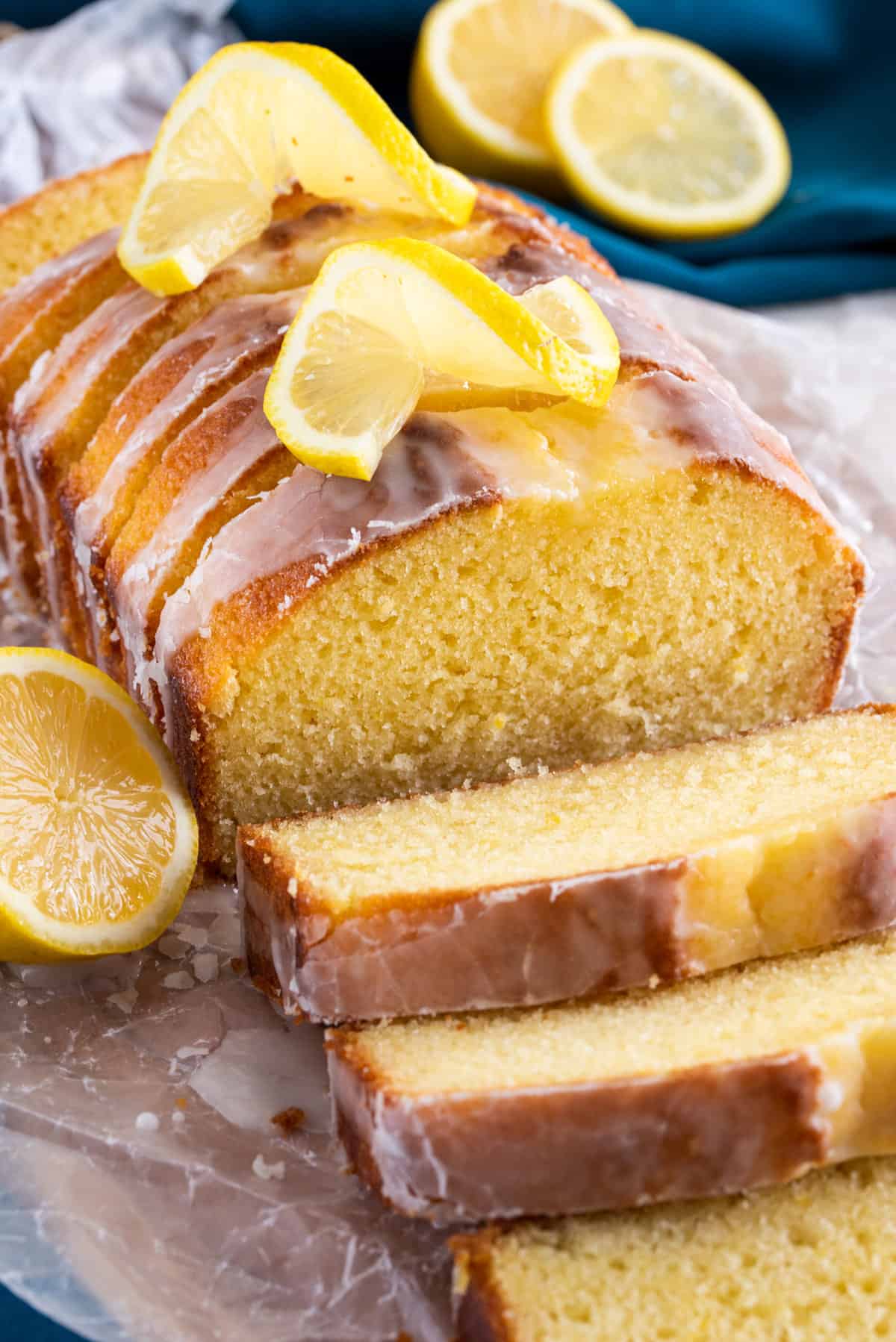 A glazed and sliced lemon cake falling away with lemons and drizzled glaze dripping around.