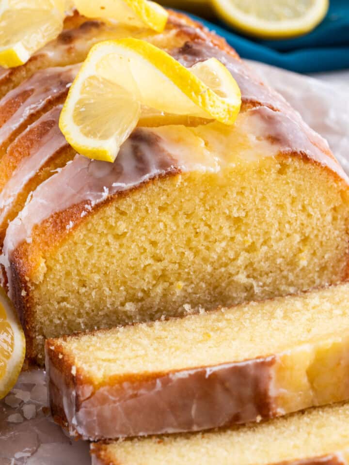 Closeup to show texture of sliced lemon yogurt cake with glaze on top and lemon curls.