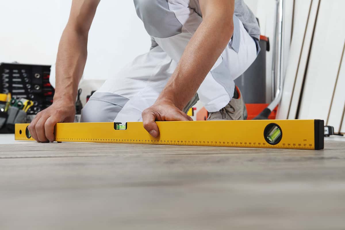 Man using a level to check for evenness and slope on a vinyl floor.