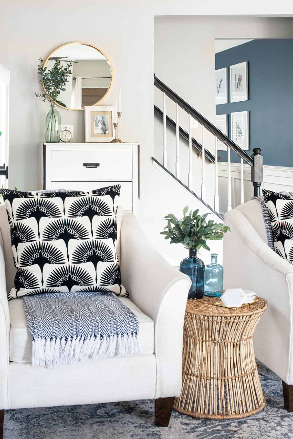 Two white accent chairs with bamboo side table in a bohemian and traditional style with staircase behind them.