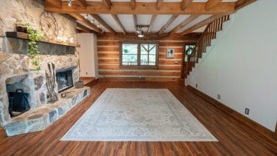 Sideview of a rustic log cabin that has a stone fireplace and large beamed ceilings in the living room.