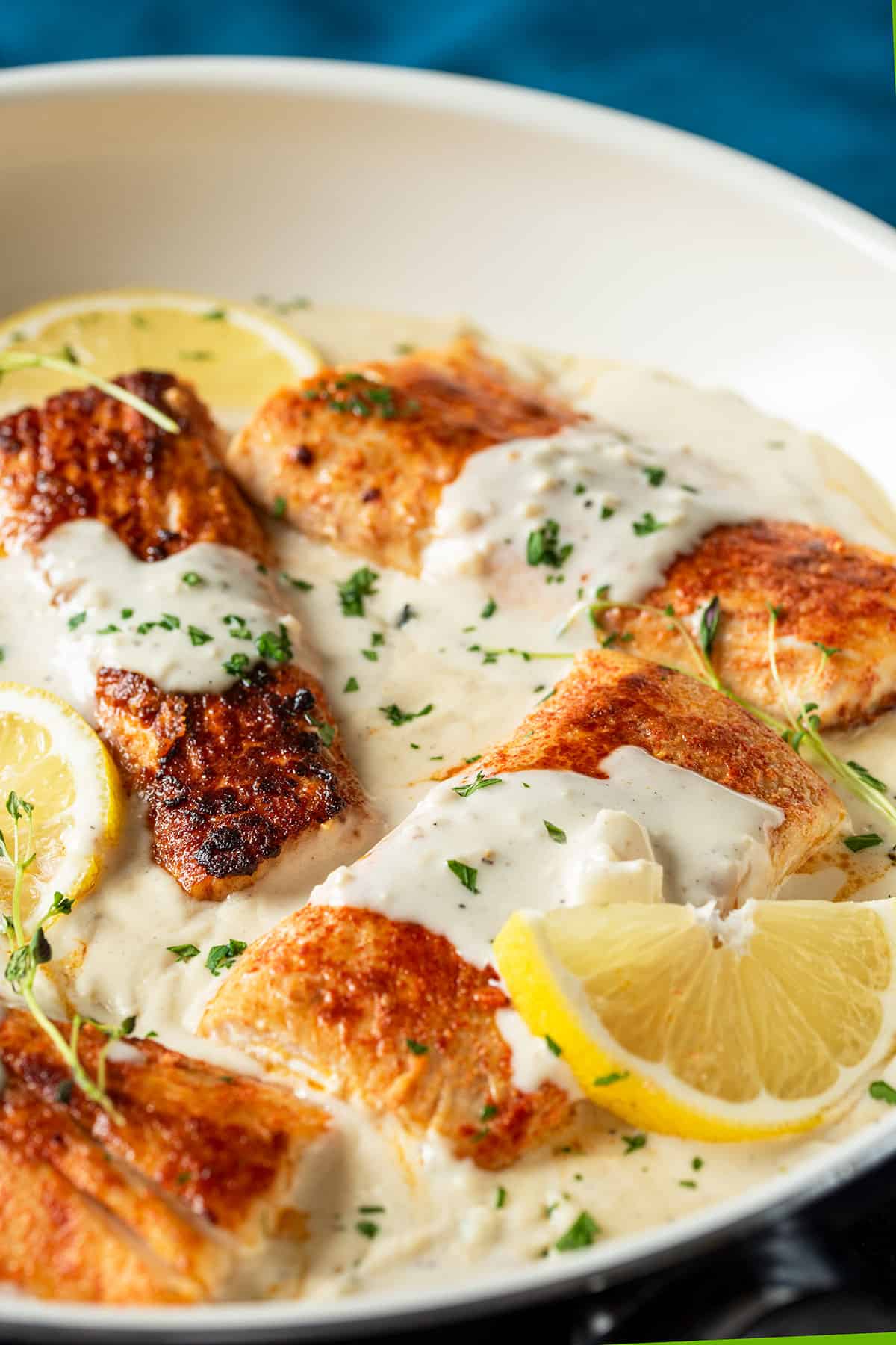 Filets of mahi-mahi in a skillet with garlic sauce, lemon slices, and fresh herbs.