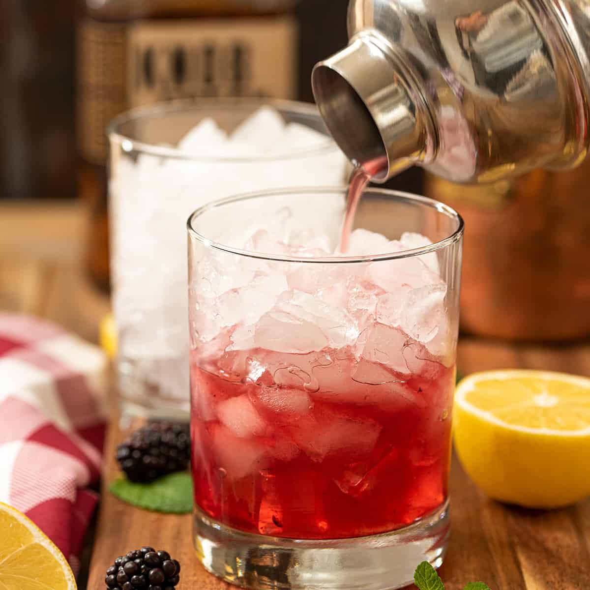 A cocktail shaker pouring red juice into a rocks glass with ice in it.