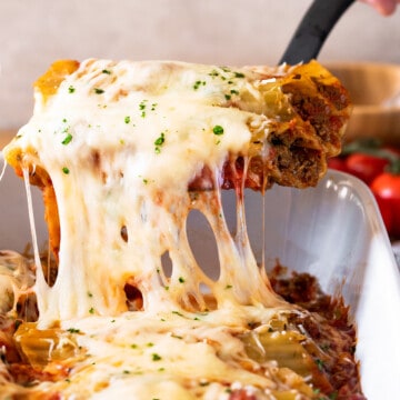 Beef Cannelloni being pulled out of pan with melted mozzarella cheese stringing.