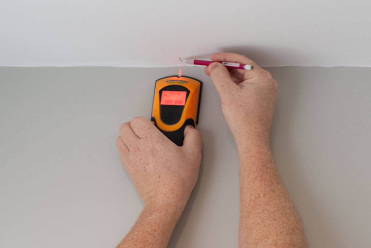 Closeup of a man using a stud finder to measure and mark wall stud locations.