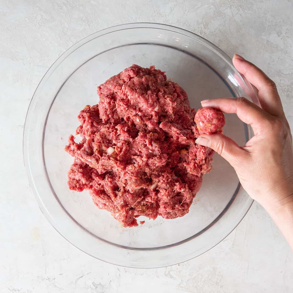 A bowl of ground beef mixture with a woman holding a single meatball.