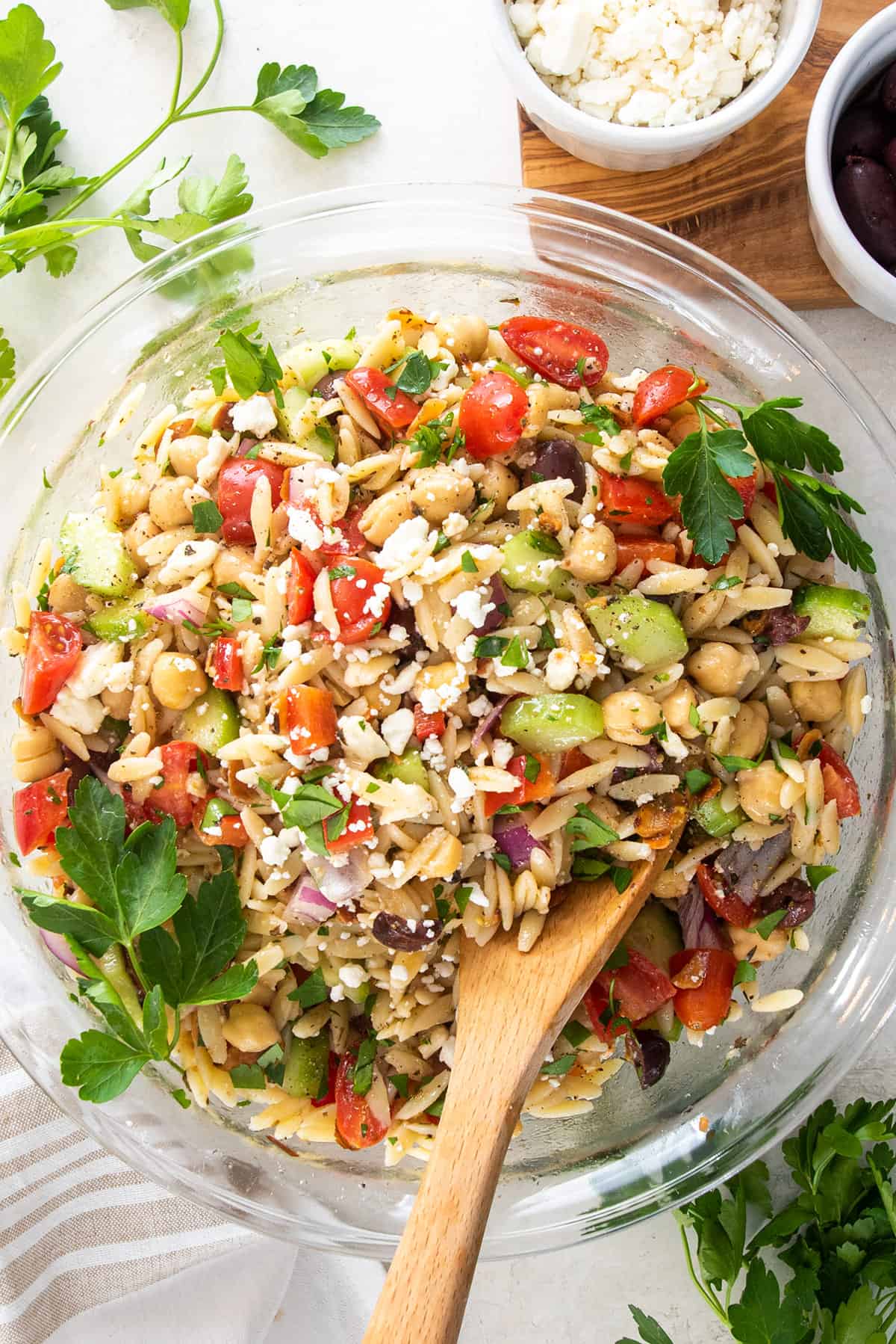Overhead view of Mediterranean orzo mixture in a glass bowl with feta and parseley sprinkled over top.