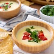 Mexican cheese dip in a small bowl garnished with tomatoes and cilantro.