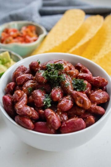 Mexican kidney beans in a bowl with taco shells in the background.