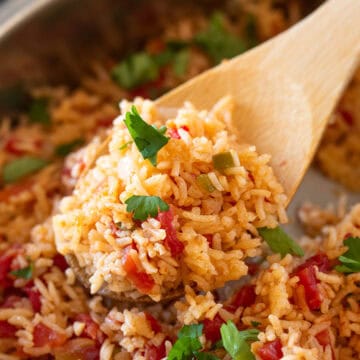 A wooden spoon serving Mexican rice with tomatoes out of a crockpot.