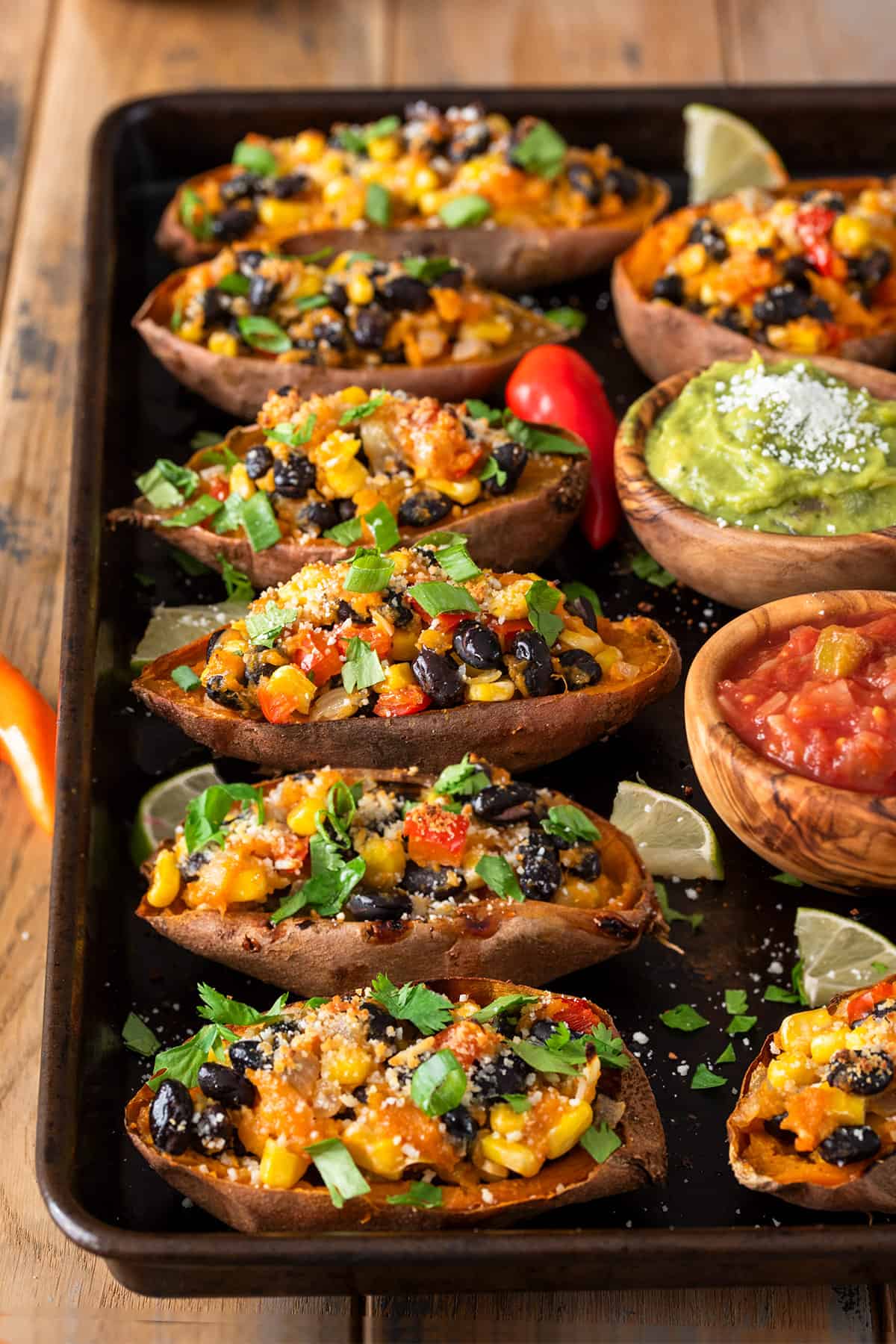 Side view of Mexican sweet potato skins on a baking sheet with salsa, guacamole, and cheese on the side.