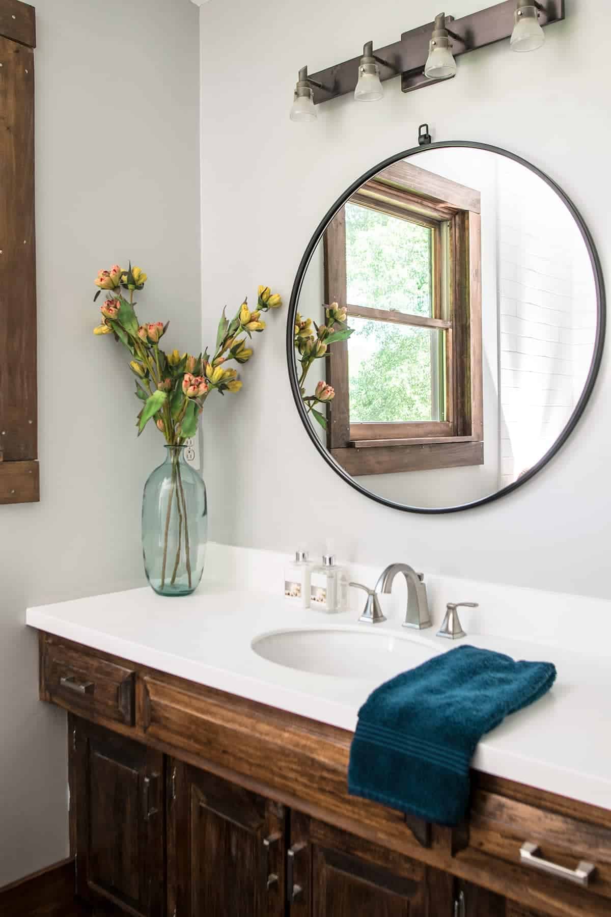 Rustic bathroom with round mirror, white countertop, dark wood cabinets, and gray walls.