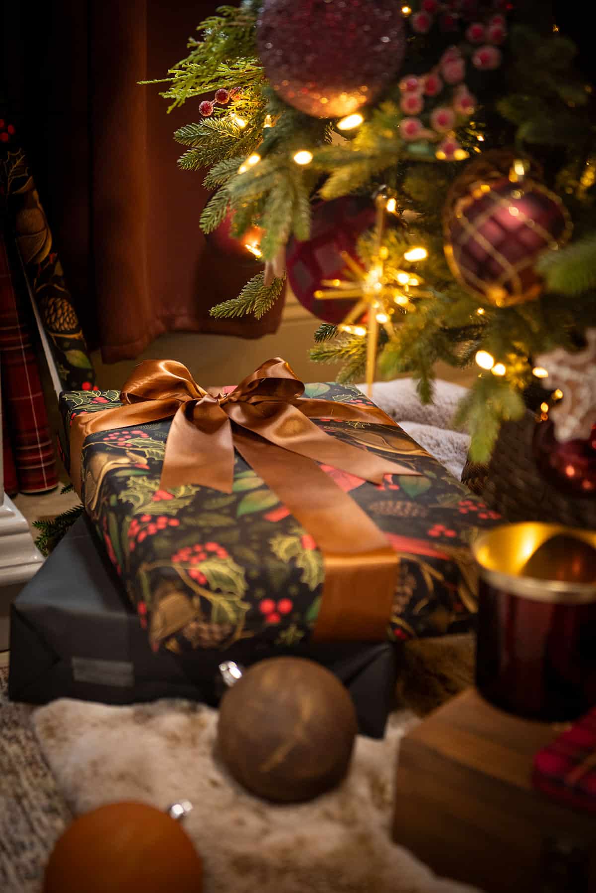 Wrapped gifts under a Christmas tree. The wrapping paper is moody cardinal bird and surrounded by ornaments and faux fur.