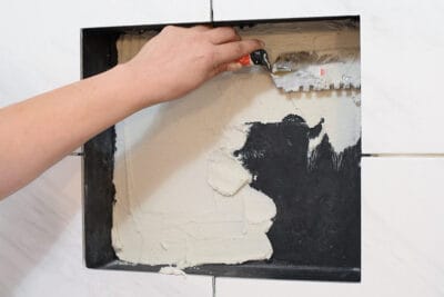 A woman adding mortar to the back of a shower niche with a mortar spreader.