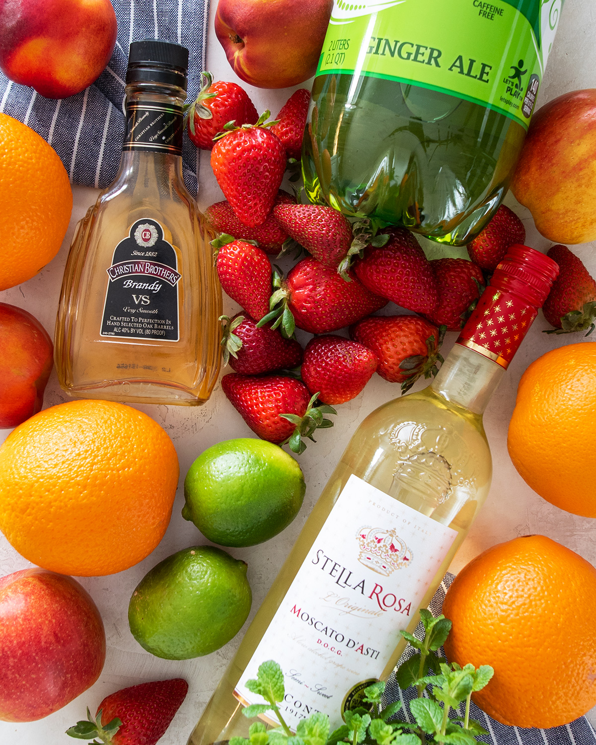 Ingredients for sweet white sangria laid out including wine, brandy, and limes, oranges, apples, and strawberry fruits.