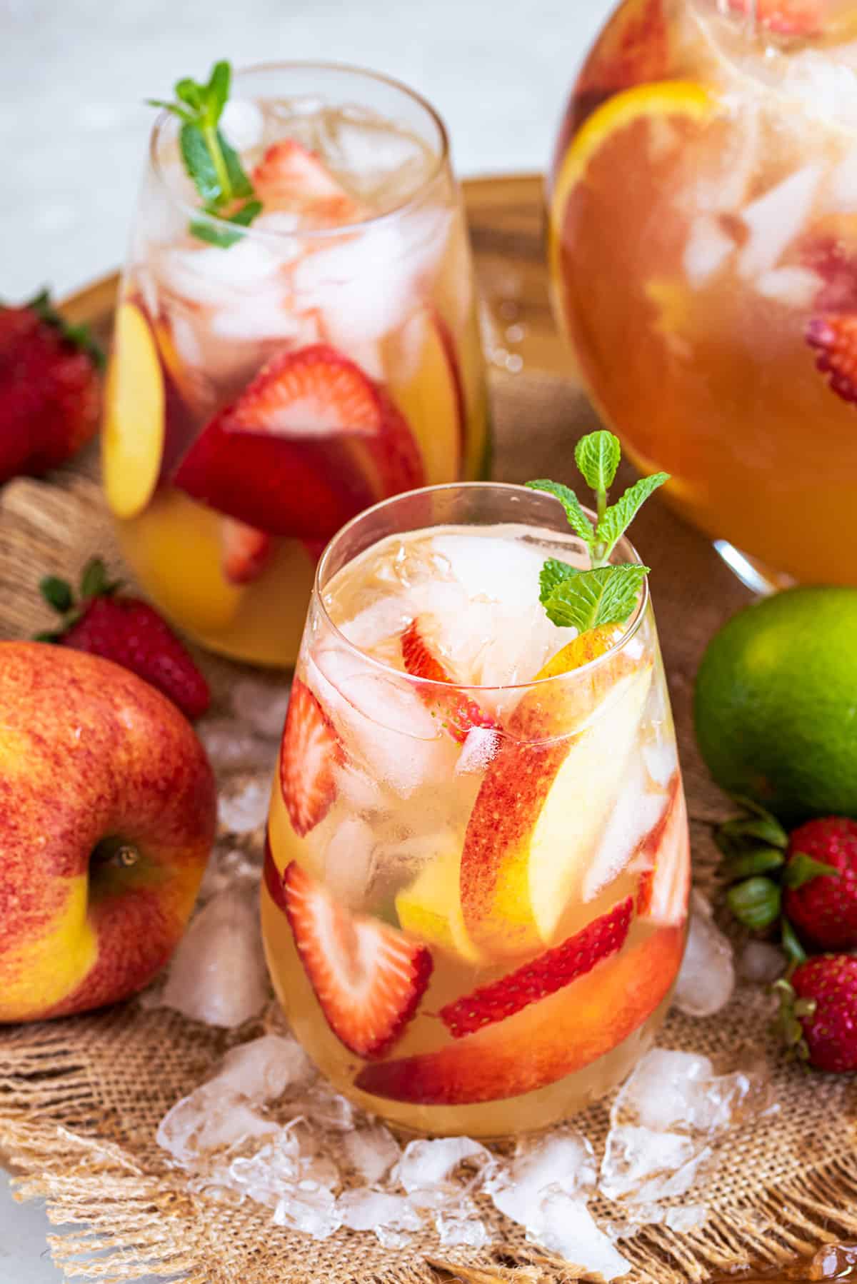 A tray with a pitcher and glasses of moscato sangria with apples sprinkled around.