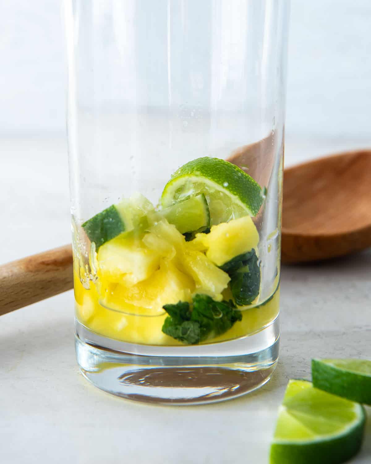 A closeup of mint leaves, pineapple, and lime slices after being muddled in a glass.