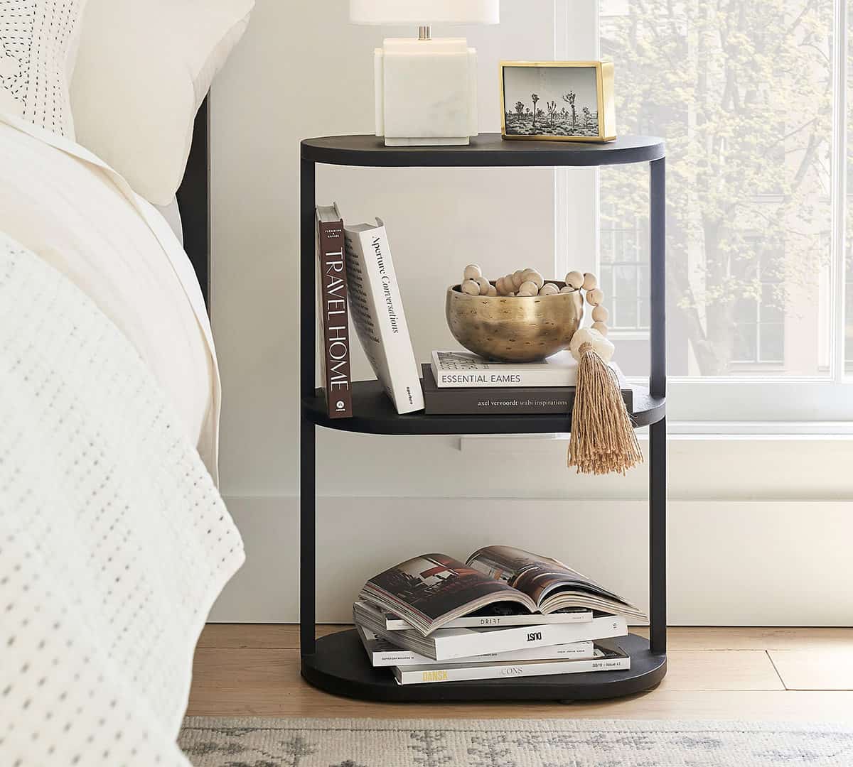 Black metal slim nightstand with 3 shelves decorated with books and bohemian bedroom decor.