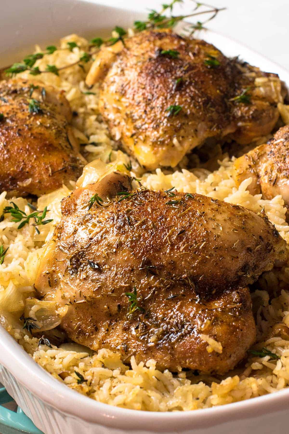 Baked chicken breasts laid atop cooked seasoned rice in a white baking dish.