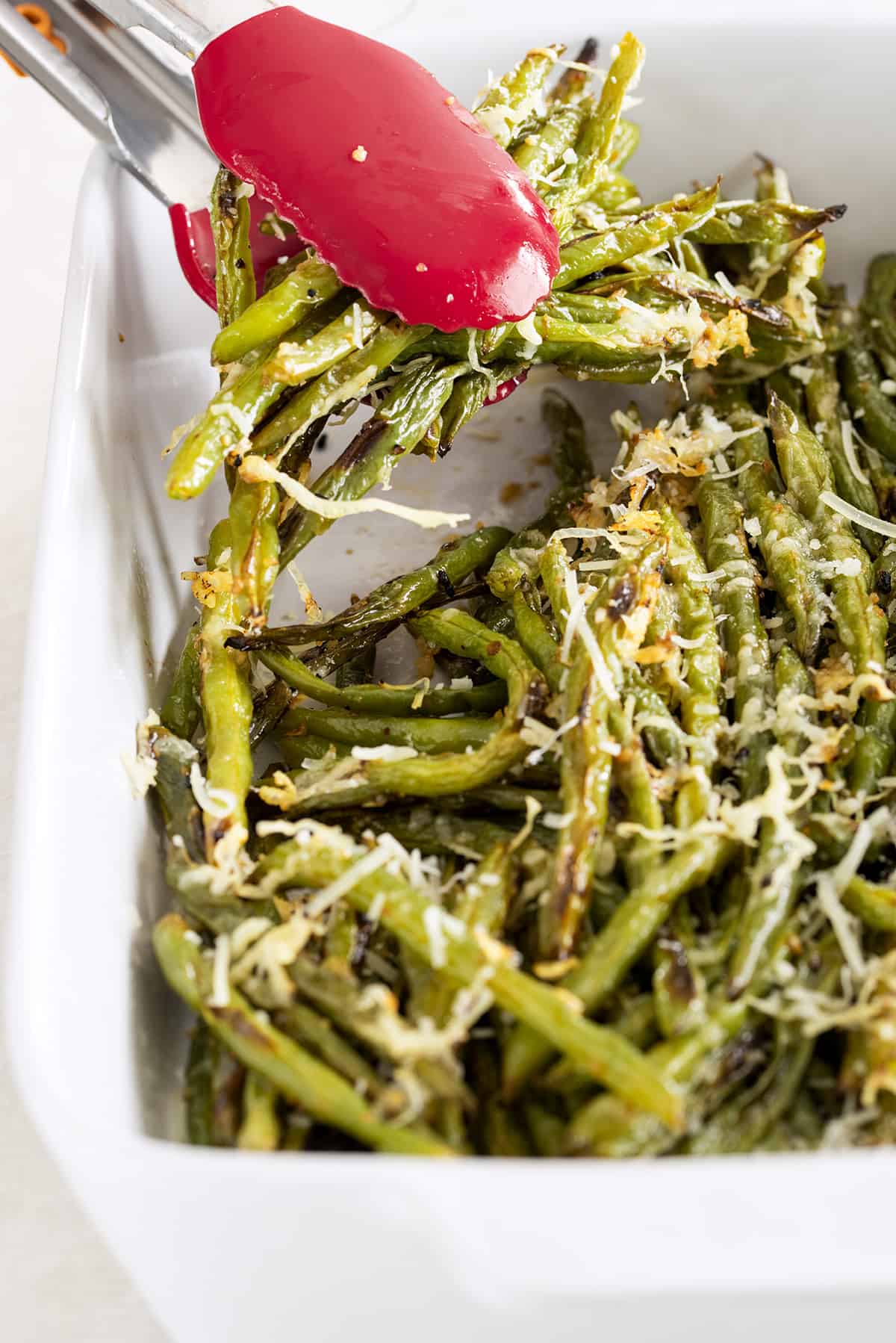 Long oven roasted green beans being served with tongs.