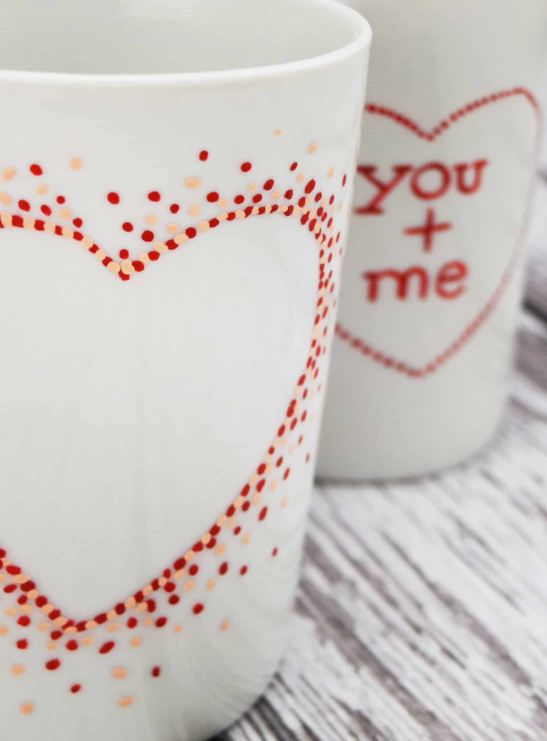 White ceramic coffee mugs with hand painted polka dot heart shapes on white wood planks.