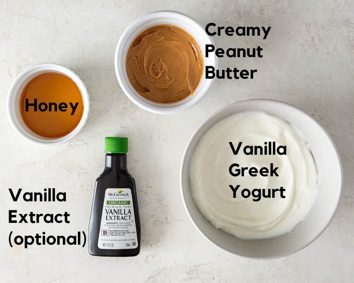 Honey, Vanilla extract, peanut butter, and vanilla Greek yogurt laid out on a table to make peanut butter dip.