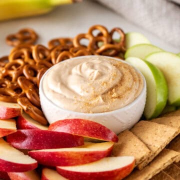Closeup of peanut butter dip in a bowl with apple slices, graham crackers, and pretzels around.