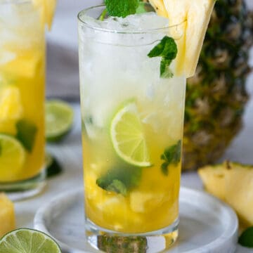 A pineapple mojito in a tall glass with lime slices and pineapple wedges as garnish.