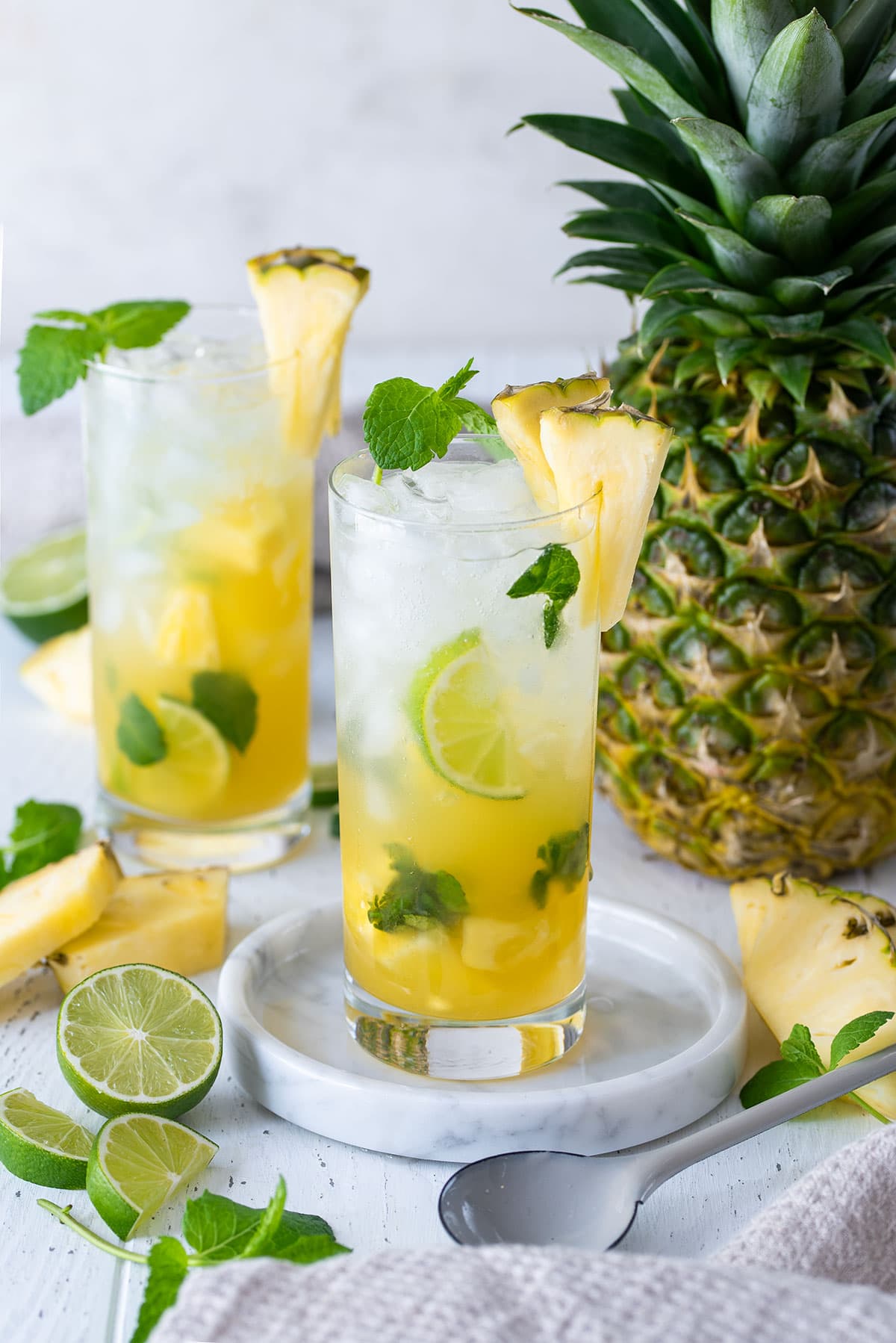 Two Pineapple Mojito Cocktails in tall glasses with limes and pineapples as garnish.