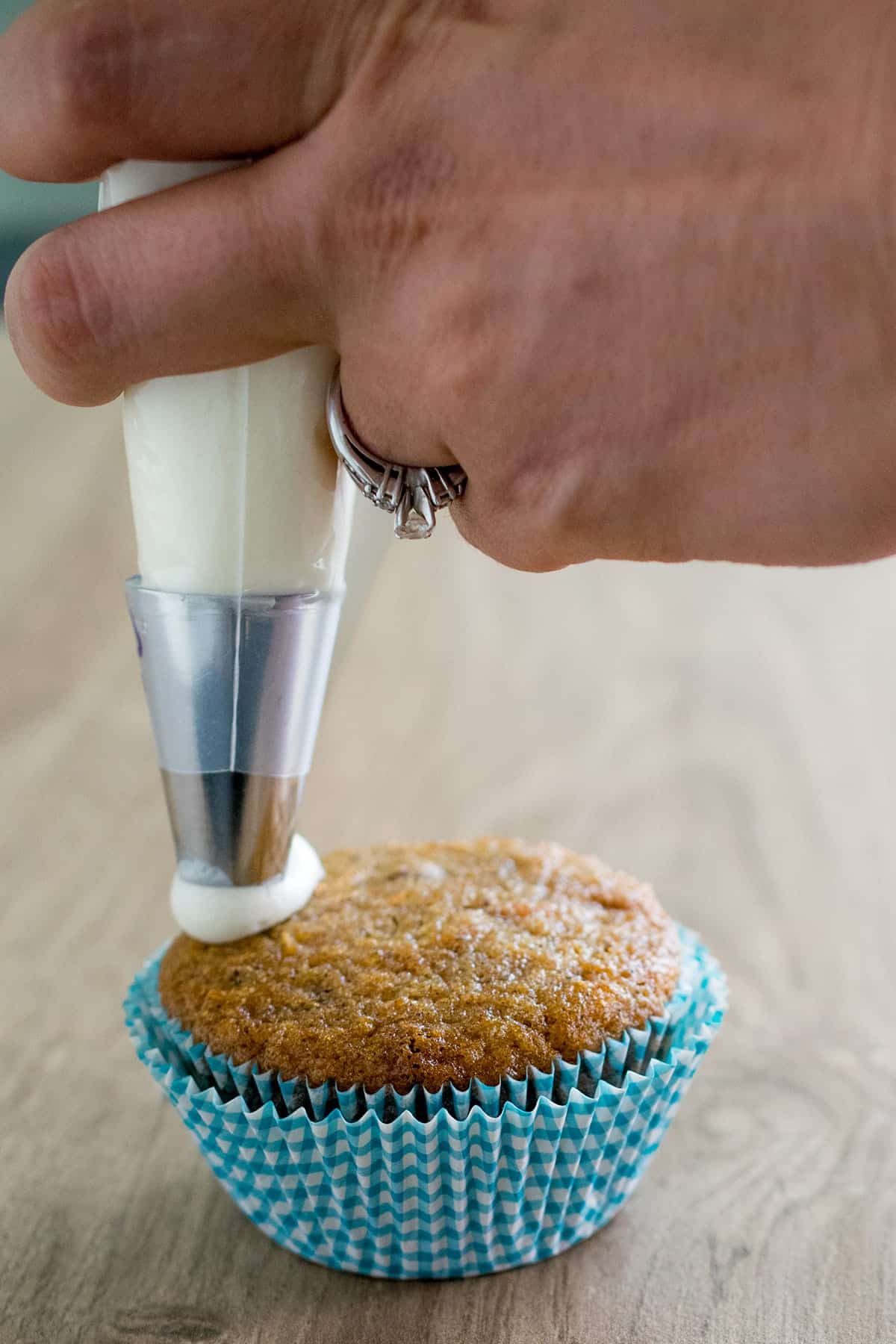 Frosting being piped on fresh baked carrot cake cupcake in blue cupcake liner