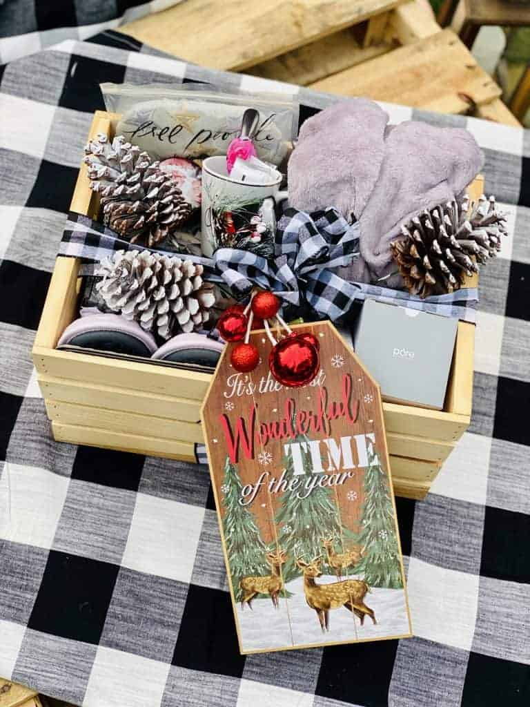 Christmas crate full of small gift items and flocked pine cones tied with black and white plaid bow.