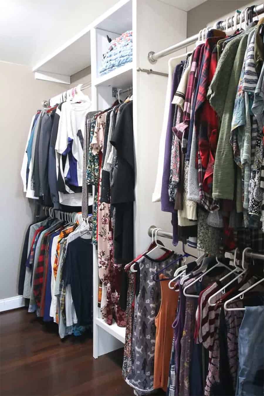 A full white closet with lots of hanging clothes.