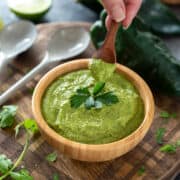 Woman picking up a spoon of poblano cream sauce in a bowl.